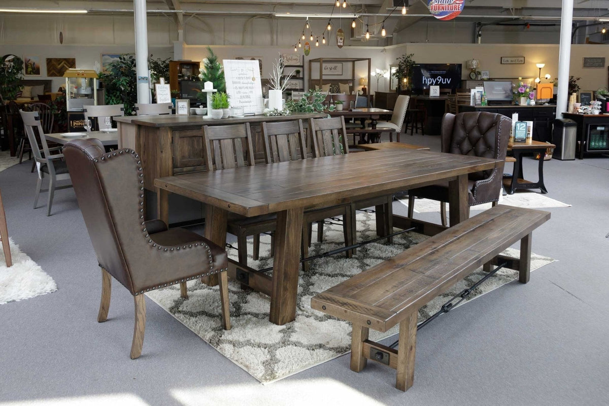 Long Ouray trestle table in the showroom with leather wing chairs at the ends, panel back side chairs and a bench