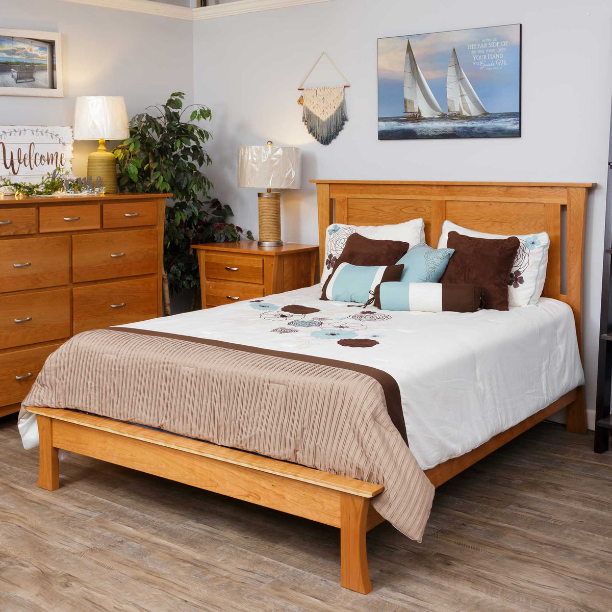 Honey toned panel bed in a showroom bedroom with a nightstand, dresser and layered blue bedding