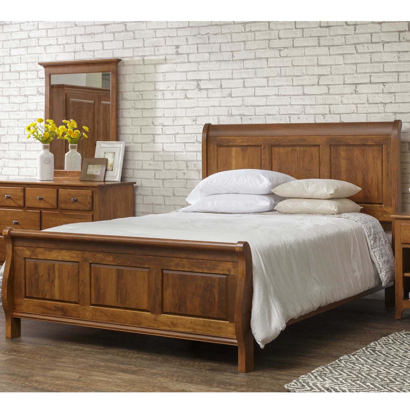 Cherry sleigh bed with paneled headboard and rolled footboard, white bedding, dresser mirror and nightstand nearby