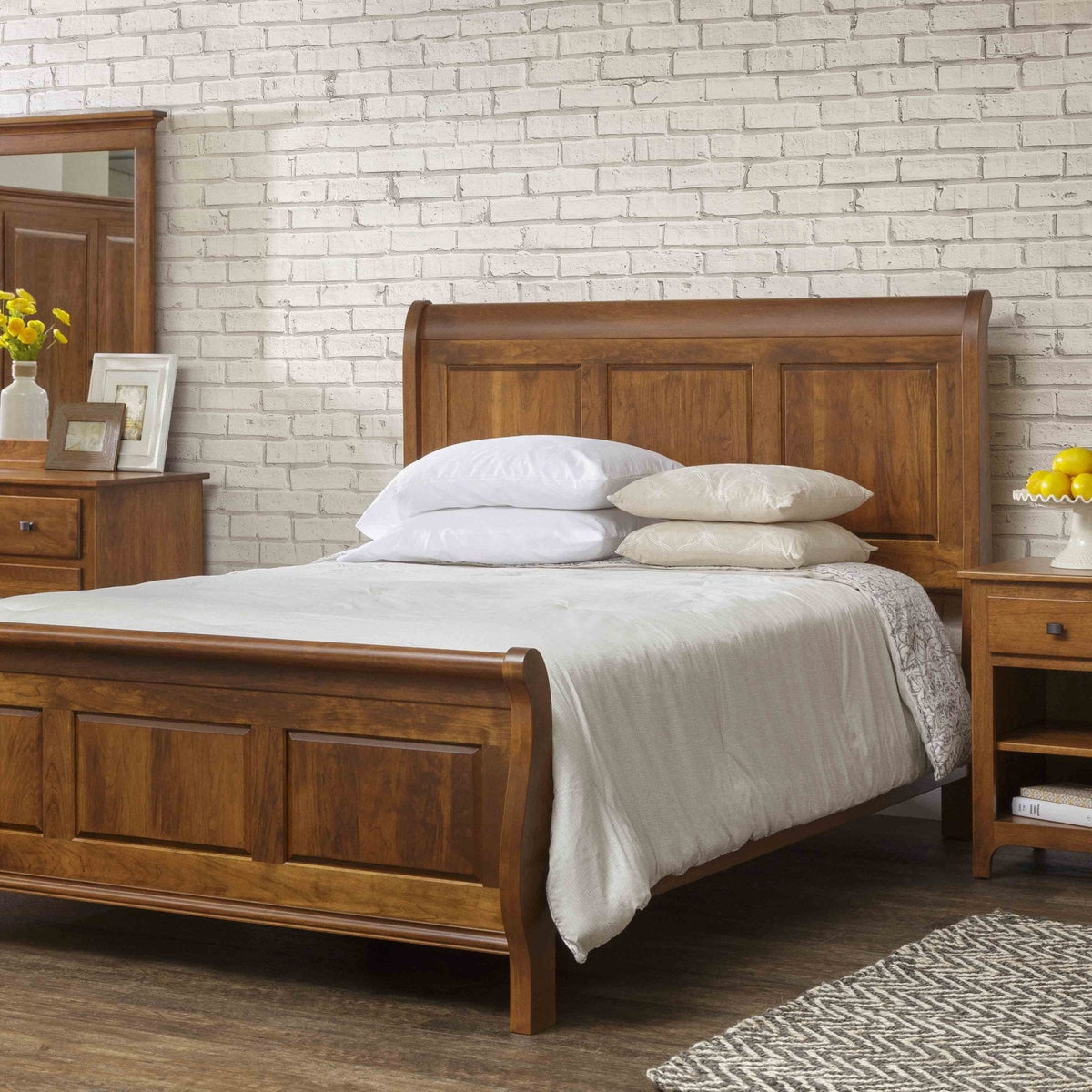 Sleigh bed in warm cherry dressed in white linens beside an open nightstand with lemons, against white brick