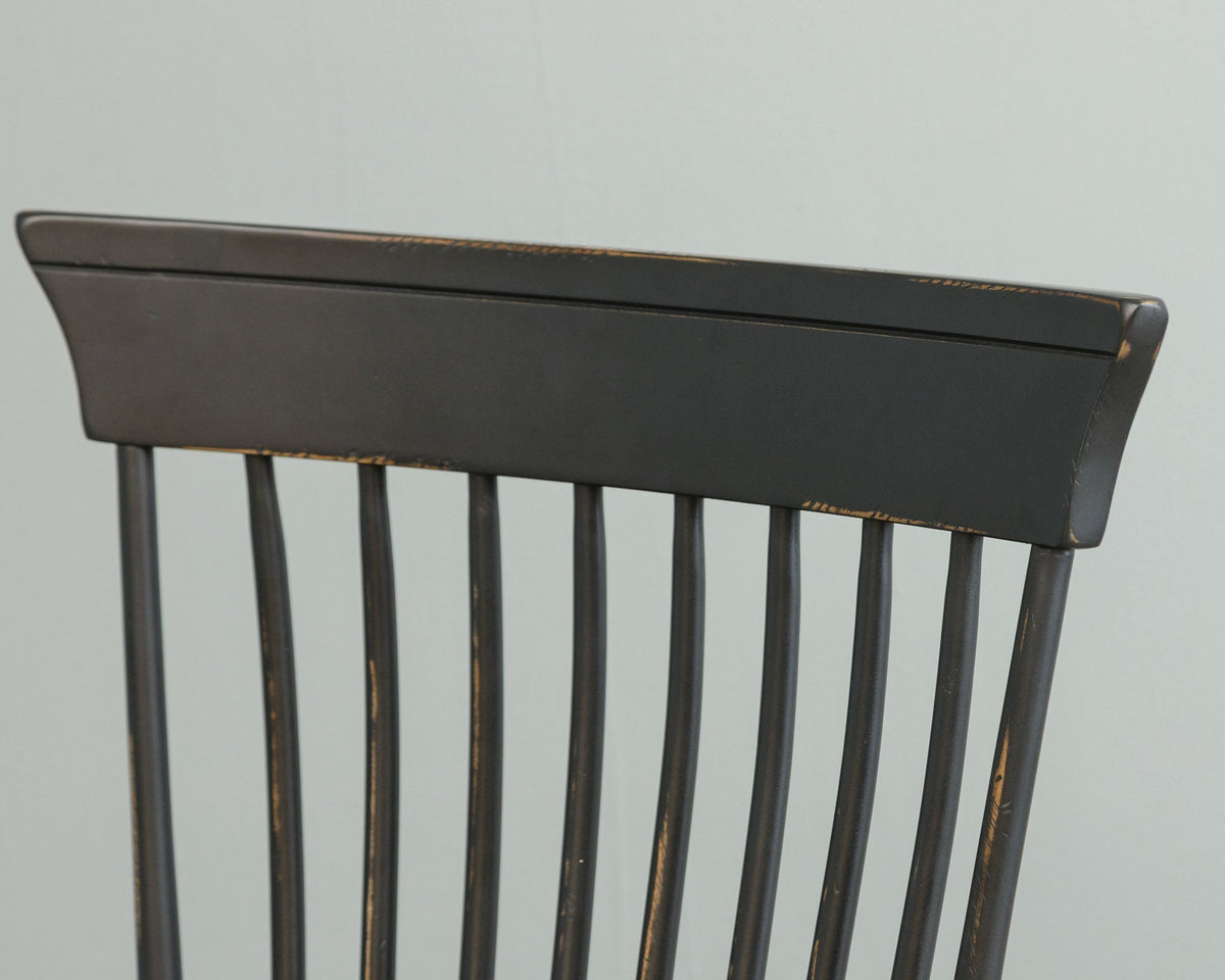 Close-up of the black Windsor chair crest rail and spindles showing worn edges over the aged painted finish