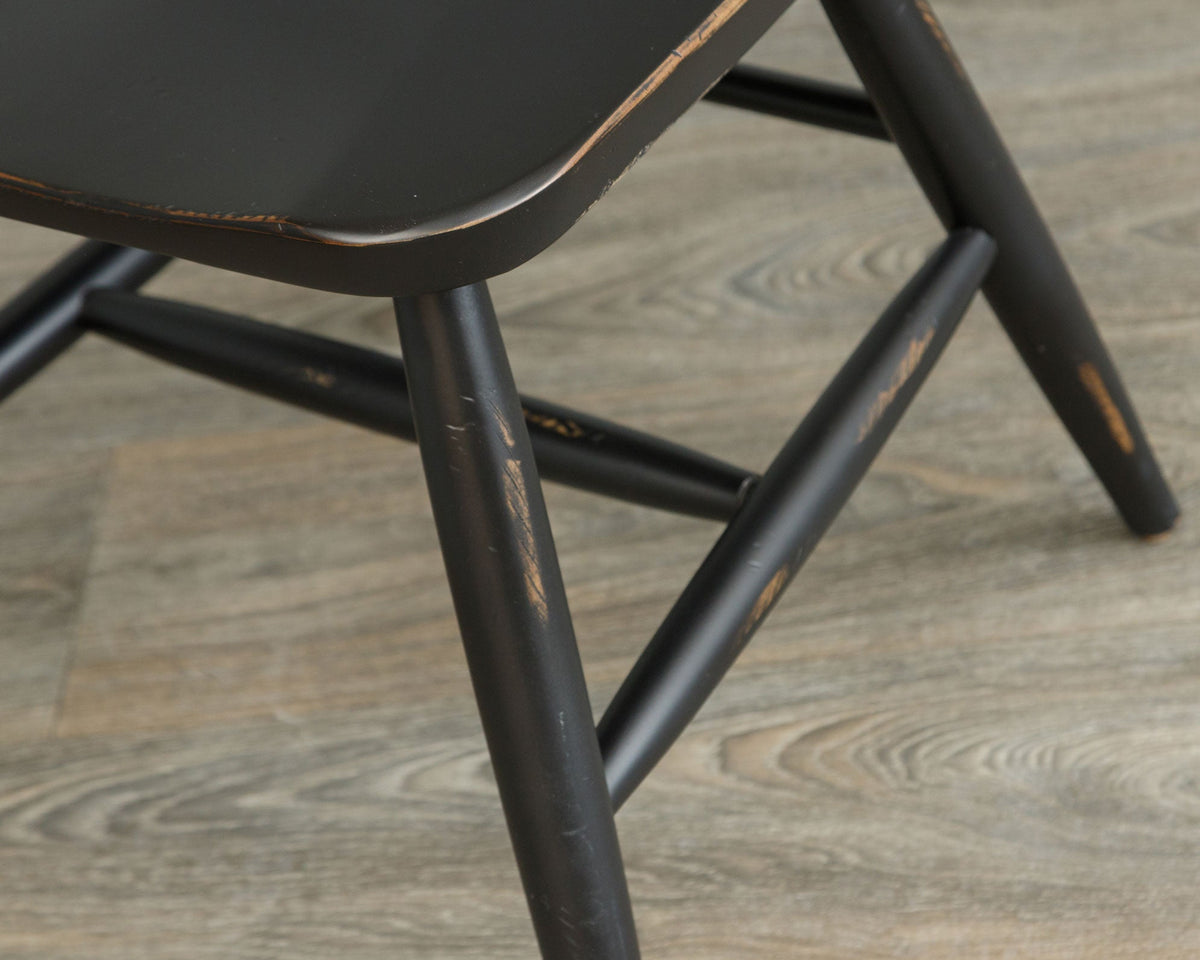 Detail of the black Windsor chair seat corner and turned legs with H stretcher and rubbed through paint