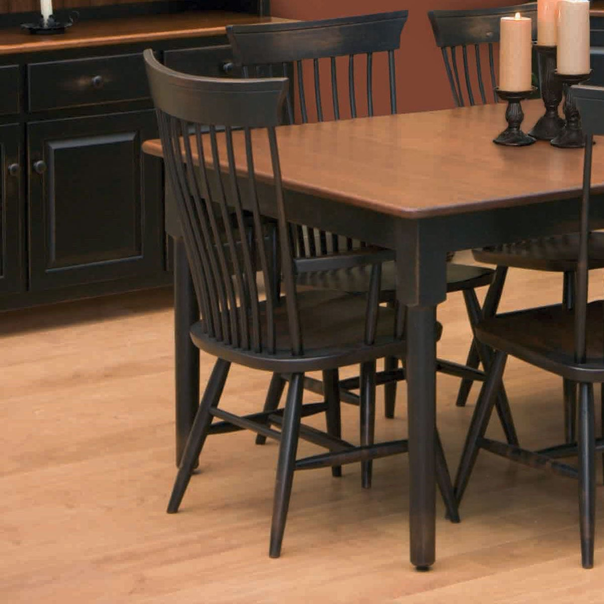 Black Windsor side chairs pulled up to an oak topped dining table with candlesticks and a black sideboard behind