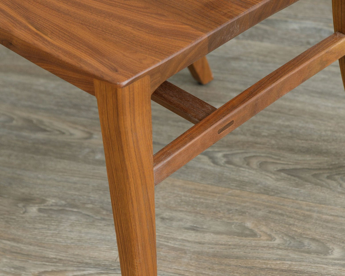 Detail of a walnut dining chair seat and tapered legs joined by mortised H stretchers