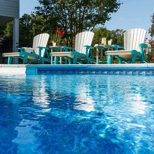 Row of driftwood and aruba blue poly chaise lounges with round side tables reflected in a sunny swimming pool