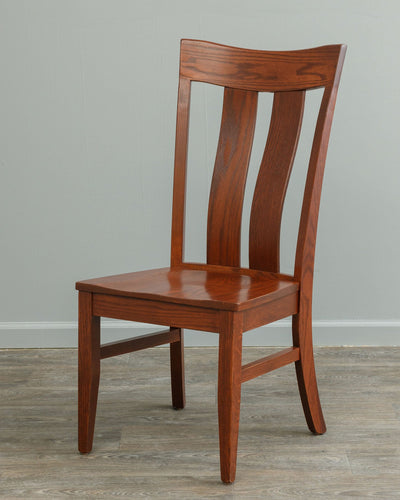 Oak lumbar dining chair with a shaped crest rail, two curved back slats and a solid saddle seat, photographed against gray