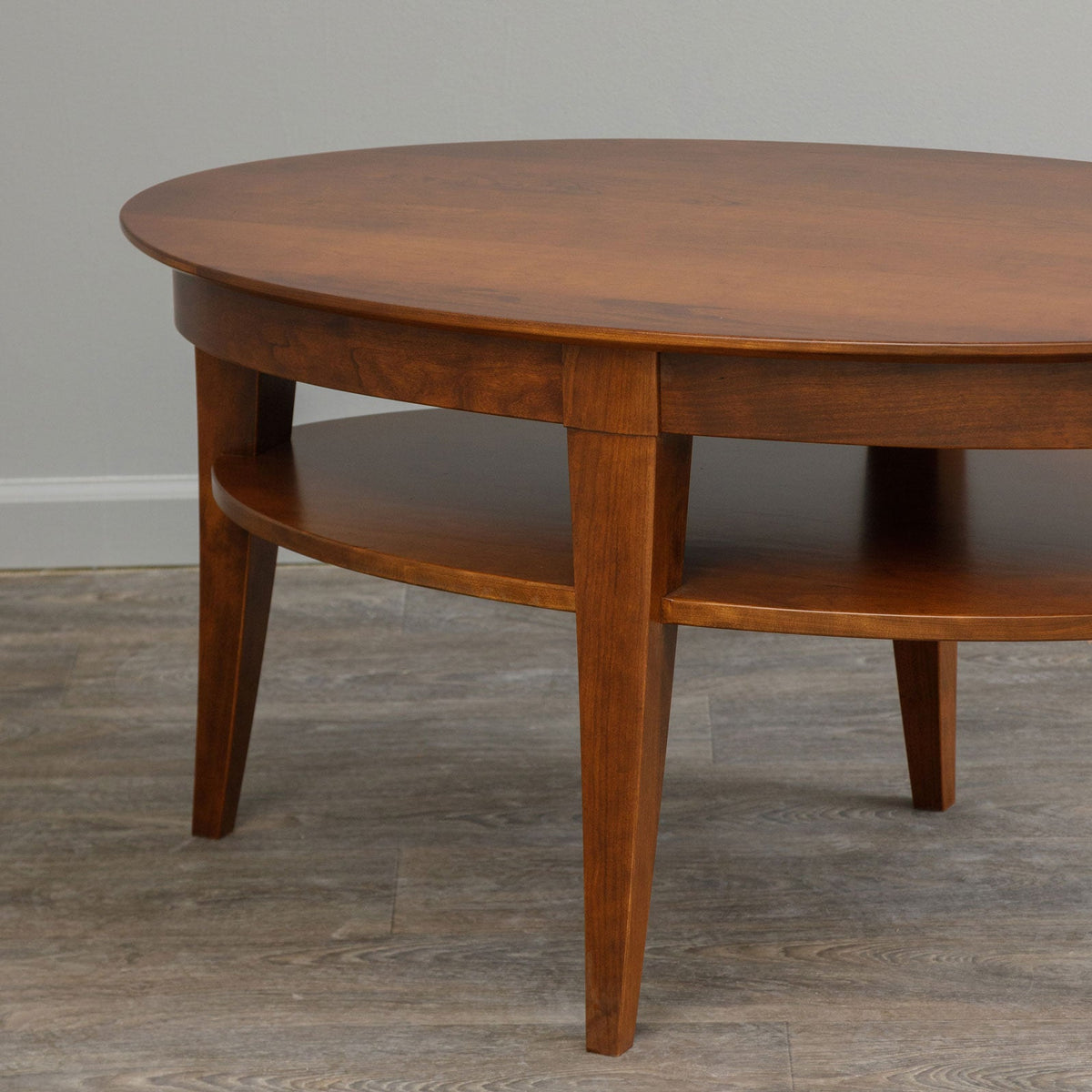 Angled view of the oval cherry coffee table showing the tapered legs, apron and curved lower shelf