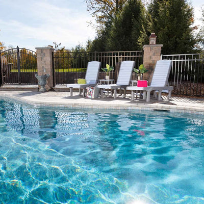 Three white and gray poly chaise lounge chairs with adjustable backs lined up along a blue swimming pool deck