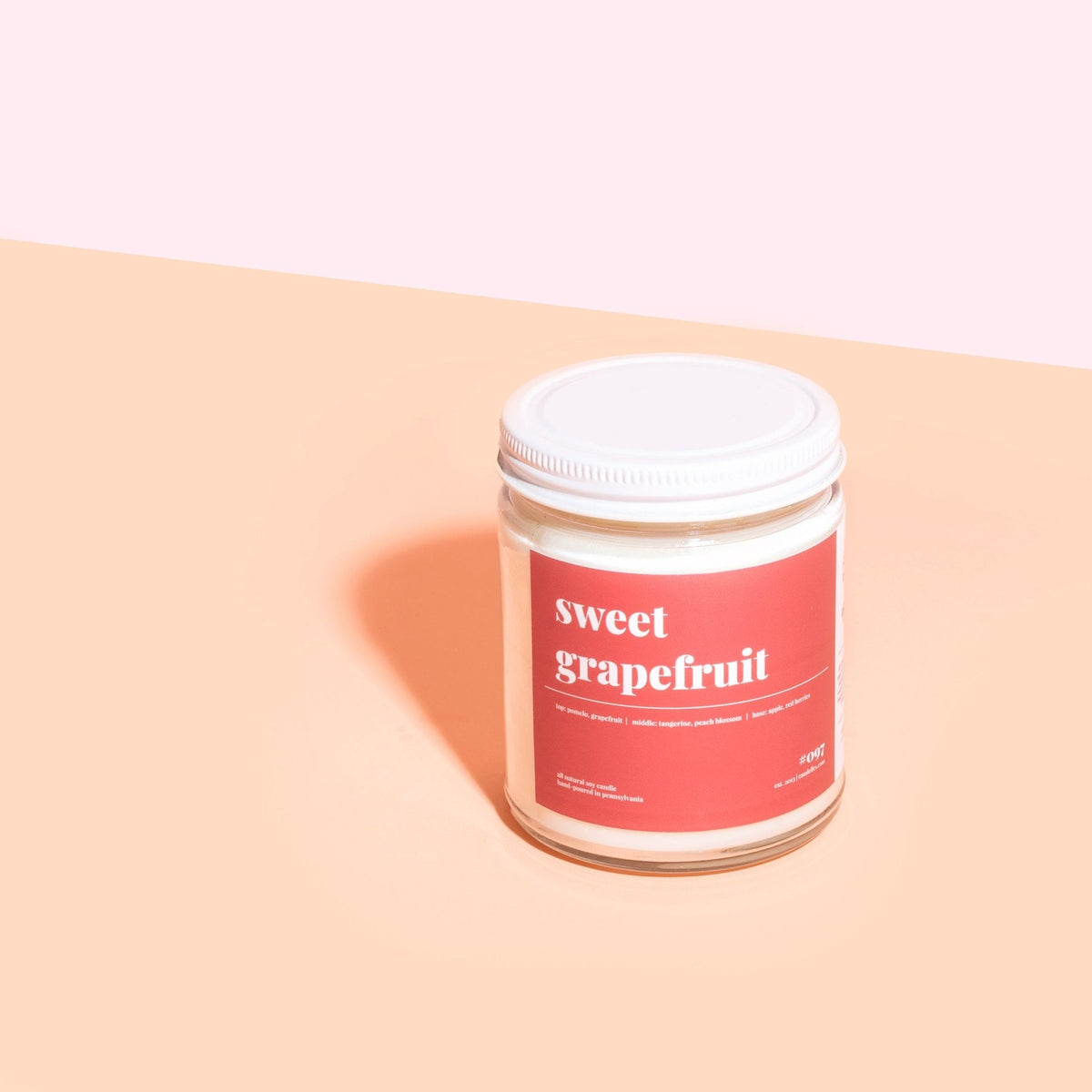 Lidded sweet grapefruit soy candle with a red label centered on a two-tone peach and pink background