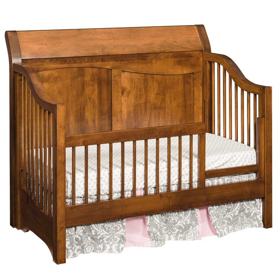 Cherry toned sleigh crib converted to a toddler day bed with rounded spindles and a curved panel headboard
