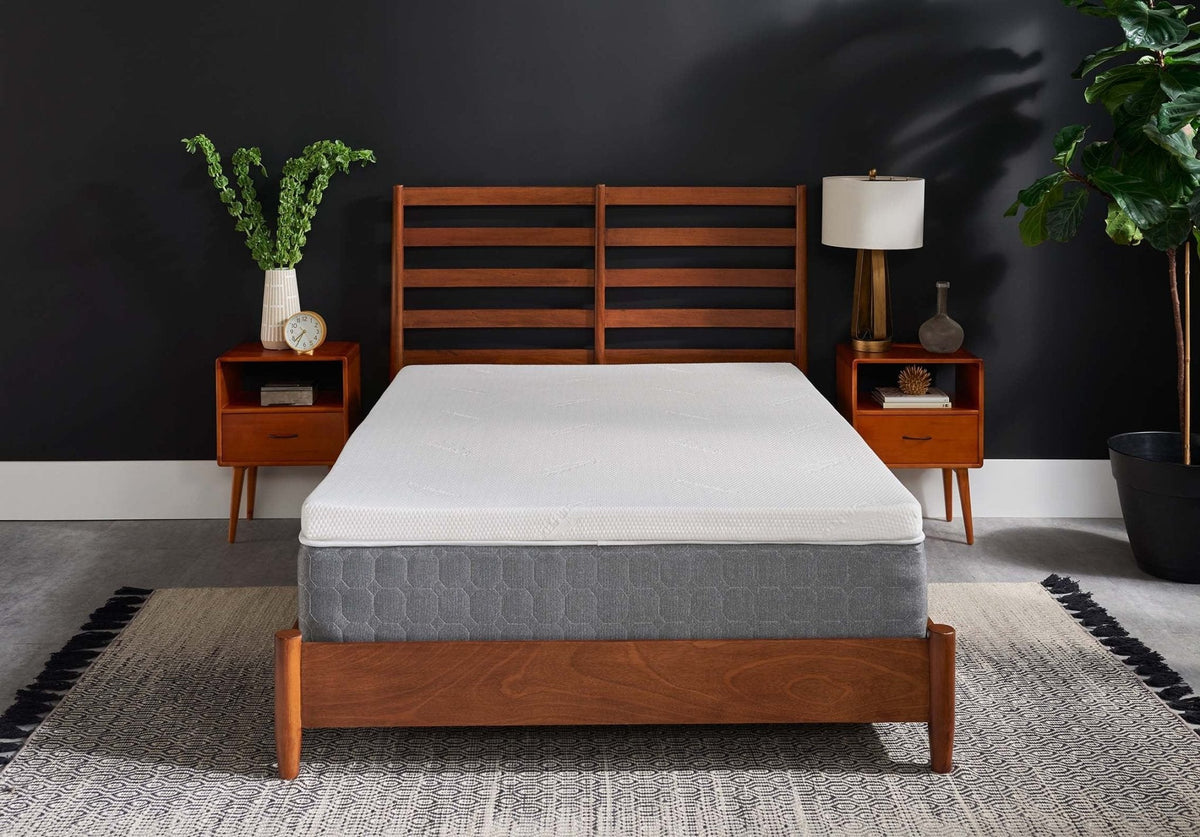 White foam mattress topper layered on a gray mattress in a wood platform bed between two mid-century nightstands
