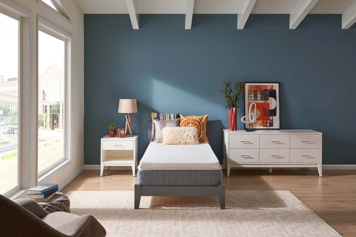 Twin bed with a white foam topper over a gray mattress in a blue and white bedroom with a dresser and nightstand