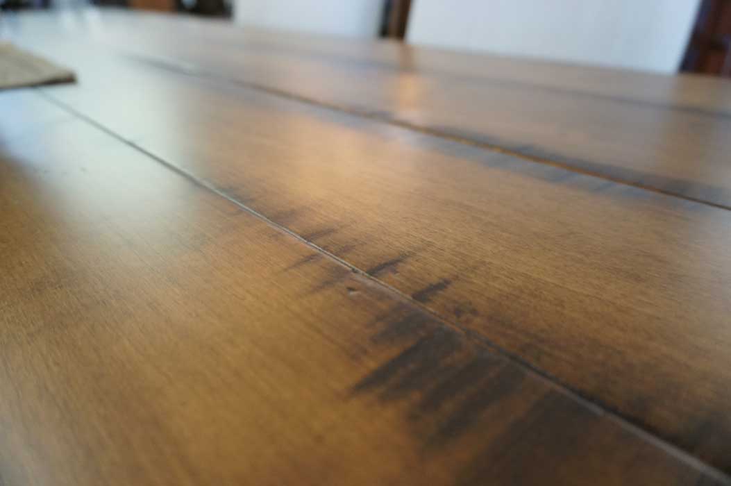 Close-up of the Westin table's distressed maple plank surface, seam line and dark antiqued markings