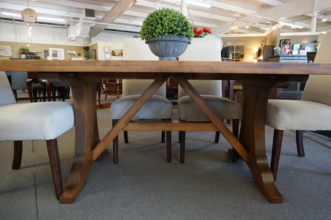 Head-on showroom view of the Westin trestle base with angled cross brace and upholstered dining chairs behind