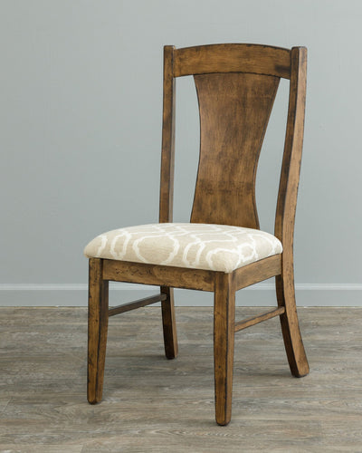 Rustic brown dining chair with a curved hourglass back panel and cream patterned upholstered seat on gray flooring