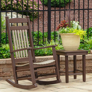Brown poly porch rocker with tan spindle back and contoured seat beside a square side table and flower pot