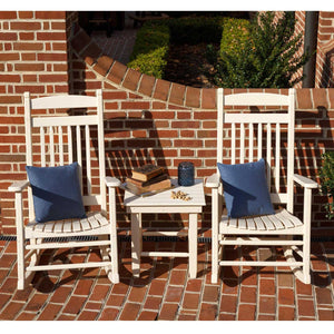 Two white poly rockers with navy pillows beside a small table holding books and a jar on brick pavers
