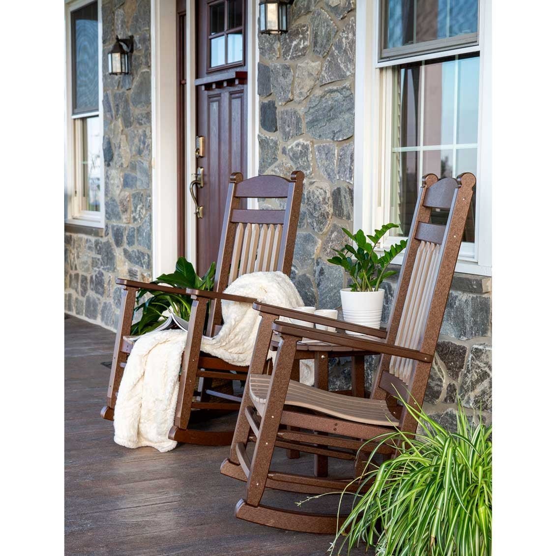 Brown and tan poly rockers with a cream throw and potted plants on a stone farmhouse front porch
