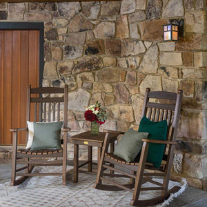 Brown poly rocking chairs with green pillows and a flower vase on a side table by a stone entryway