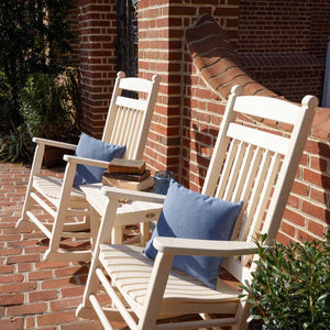 Ivory poly porch rockers with blue pillows, stacked books and a candle on a side table by a brick wall
