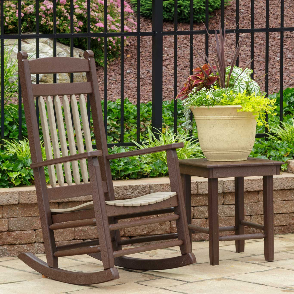 Brown poly rocker with tan spindle back next to a side table holding a large flowering planter